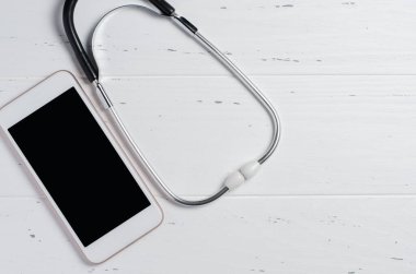 Beyaz arka planda akıllı telefon ve steteskop. İnternet eczanesi ya da teletıp konsepti. Boşluğu kopyala.