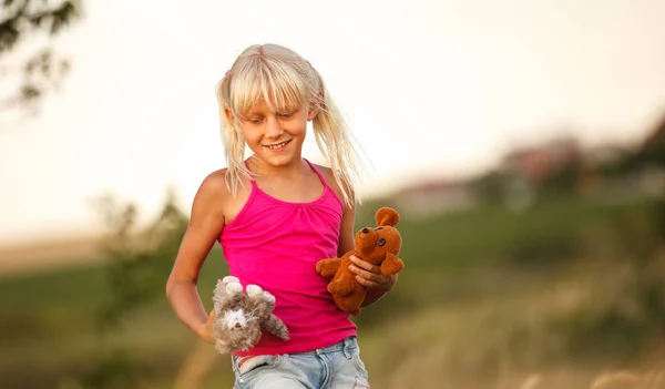 Piękna dziewczynka blondynka z miękkimi zabawkami w polu w lecie — Zdjęcie stockowe