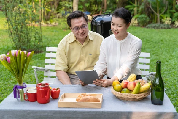 An elderly couple is sitting watching the screen tablet