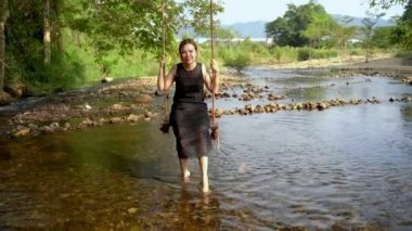 nehir boyunca bir salıncak üzerinde oturan kadın ayaklarını su ile yavaş yavaş ve mutlu bir şekilde rahatlatıcı bir günde salıncak.