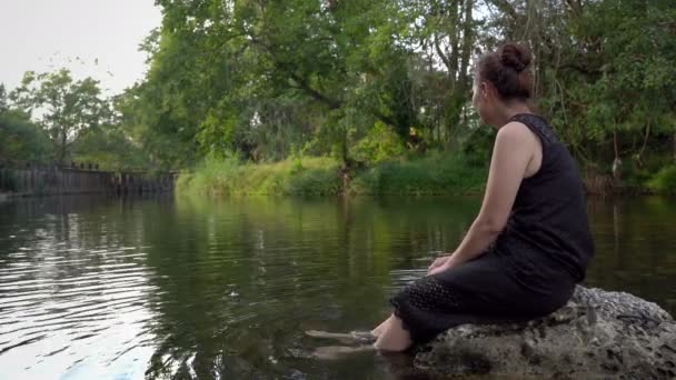 ストリームに沿ってブランコに座っている女性スイング水を介して足ゆっくり 楽しくリラックスした日に — ストック動画