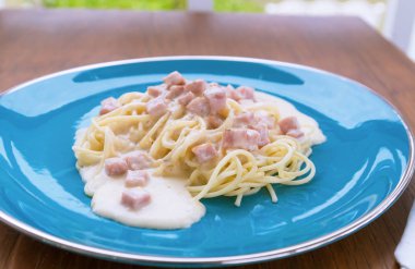 Spagetti Carbonara ahşap bir masa üzerinde mavi bir tabakta pastırma ve peynir ile.