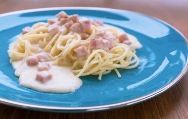 Spagetti Carbonara ahşap bir masa üzerinde mavi bir tabakta pastırma ve peynir ile.