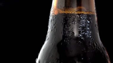 Siyah arka planda bir şişe soğuk siyah biranın makro rotasyon video çekimi.