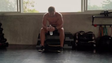 Spor salonunda egzersiz yapan yakışıklı bir delikanlının güzel vücut şekli. O dinleniyor ve pencerenin yanındaki spor salonunda su içiyor..