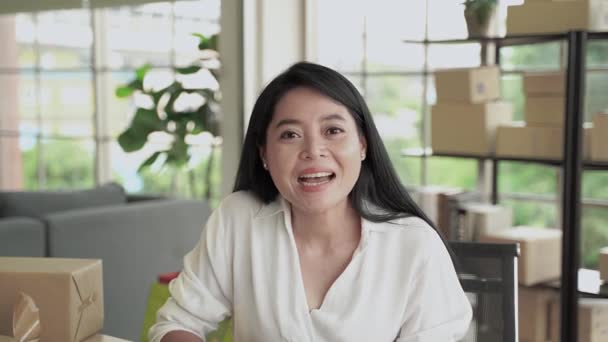 中年のアジアの女性は ビデオ通話を通じて挨拶しています 彼女はソーシャルメディアを介してオンラインでビジネスを行っています — ストック動画
