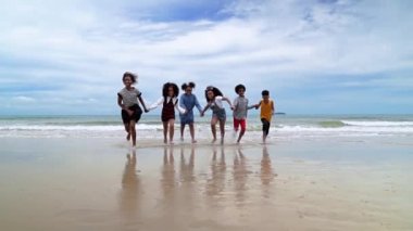 Ağır çekimde, Afrikalı-Amerikalı çocuklar yazın kumsalda el ele koşuyorlar.