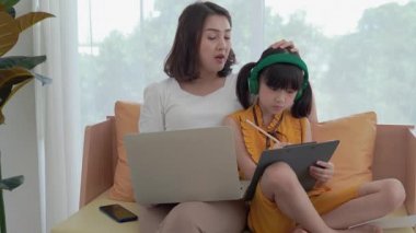 Anne, kızına oturma odasındaki kanepede rahat bir atmosferde bilgisayar kullanarak ders veriyor..