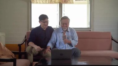 Yaşlı baba ve oğlu evlerinde dizüstü bilgisayarlarında açılan bir karaokenin mikrofonunu söylerken eğleniyorlar..