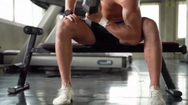 Bir adam spor salonunda dambılı kaldırarak egzersiz yapıyor..