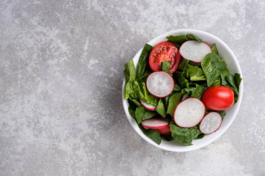Yeşil ıspanak yaprakları ile taze bahar salatası, turp, gri taş arka plan üzerinde domates.