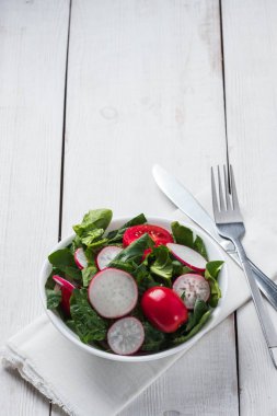 Gri taş arka planda Arugula, ıspanak, pancar, turp, salatalık ve domates yeşil yaprakları ile taze bahar salatası.
