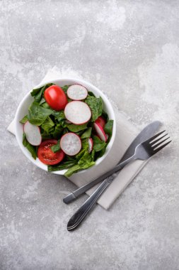Gri taş arka planda Arugula, ıspanak, pancar, turp, salatalık ve domates yeşil yaprakları ile taze bahar salatası.