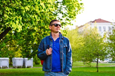 Siyah kıvırcık saçlı, güneş gözlüğü takan çekici genç adam güneşli bir günde sokakta yürüyor. Sıradan kıyafetler giyen sakallı hippi, hafta sonları dinlenmeyi sever..