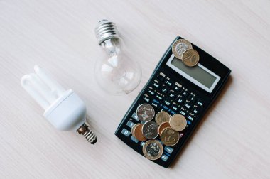 Kesilmiş görüş açısı ve hesap makinesinin yanındaki floresan lambaları beyaz enerji verimliliği kavramına izole edilmiş ellerde. Beyaz arkaplanda enerji tasarrufu lambası ve hesap makinesi