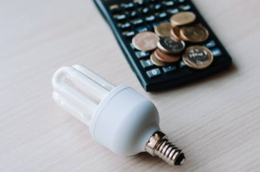 Kesilmiş görüş açısı ve hesap makinesinin yanındaki floresan lambaları beyaz enerji verimliliği kavramına izole edilmiş ellerde. Beyaz arkaplanda enerji tasarrufu lambası ve hesap makinesi