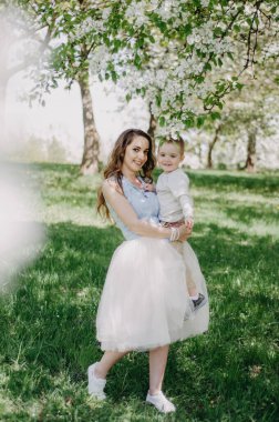 Genç bir anne ve küçük oğlu güneşli bir günde bahar parkında yürürler.