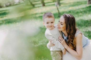 Küçük oğluyla oynayan ve onunla eğlenen mutlu genç bir anne. Bahar ya da yaz günlerinde. Elma bahçesinde ya da parkta güzel bir gün batımı ışığı. Mutlu aile görüşü