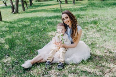 Küçük oğluyla oynayan ve onunla eğlenen mutlu genç bir anne. Bahar ya da yaz günlerinde. Elma bahçesinde ya da parkta güzel bir gün batımı ışığı. Mutlu aile kavramı. Annesiyle parkta oynayan sevimli, neşeli bir çocuk.