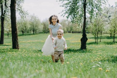 Küçük oğluyla oynayan ve onunla eğlenen mutlu genç bir anne. Bahar ya da yaz günlerinde. Elma bahçesinde ya da parkta güzel bir gün batımı ışığı. Mutlu aile kavramı. Annesiyle parkta oynayan sevimli, neşeli bir çocuk.