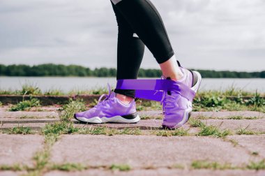 Genç esmer kadın, pembe tayt giyiyor, yaz sabahı stadyumda antrenman yapıyor. Bacakları yakından çek, dayanıklılık bandıyla güç egzersizleri yap. Sağlıklı yaşam tarzı kavramı.