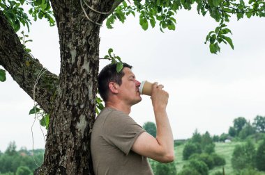 Genç adamın sabahın erken saatlerinde güneşli parkta kahve alıp götürdüğü yakın plan, bulanık arka plan.