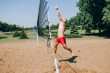 Plaj voleybolu oynayan bir adam açık mavi gökyüzünün altında topun peşinden dalıyor.