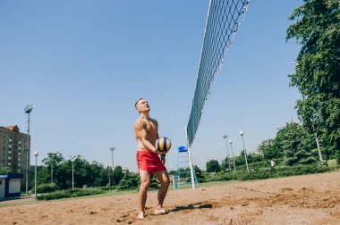Plaj voleybolu oynayan bir adam açık mavi gökyüzünün altında topun peşinden dalıyor.