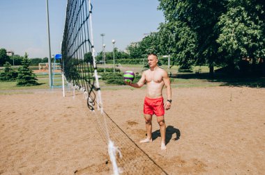 Plaj voleybolu oynayan bir adam açık mavi gökyüzünün altında topun peşinden dalıyor.