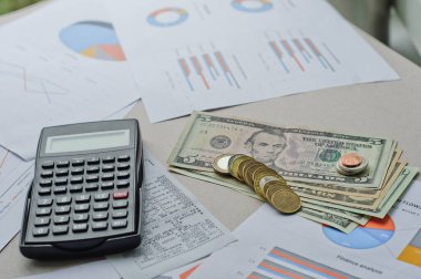 Dolarlar, hesap makinesi, loupe, kalemler ve defterler evrakların üzerinde. Ofis malzemeleri masanın üzerinde. Ofis malzemeleri mali beyanlarda yatıyor. 