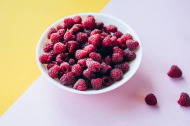 Sarı zemin üzerinde ahududu, böğürtlen ve böğürtlen bulunan güzel bir açık mavi meyve kasesi.