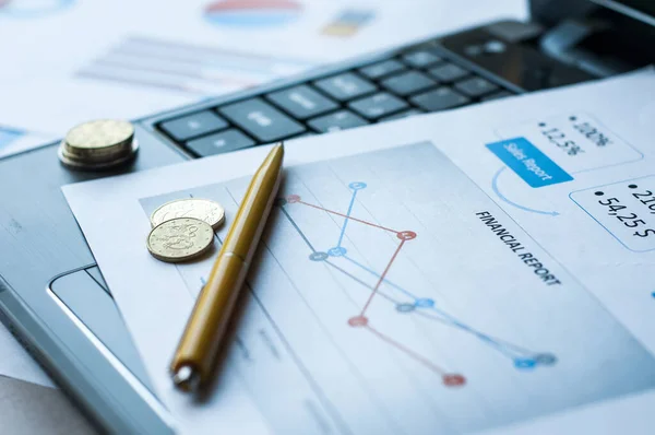 Masadaki dizüstü bilgisayarların, madeni paraların, kağıtların, gözlüklerin, kalemlerin ve hesap makinelerinin seçici odağı