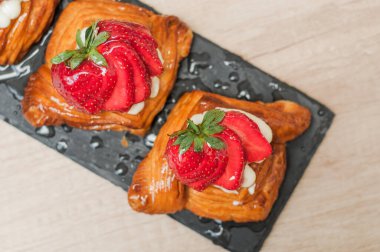 Kremalı Danimarka pastası ve siyah tabakta çilek.