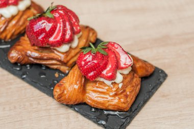 Kremalı Danimarka pastası ve siyah tabakta çilek.