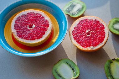 Palmiye yapraklarındaki organik tropikal meyvelerin üst görüntüsü, turuncu ve gri arka planda meyve suyu bulunan greyfurt dilimleri