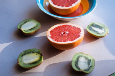 Palmiye yapraklarındaki organik tropikal meyvelerin üst görüntüsü, turuncu ve gri arka planda meyve suyu bulunan greyfurt dilimleri