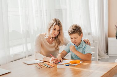 Gülümseyen anne, sevimli oğluna evde ödevlerini yapmasına yardım ediyor.