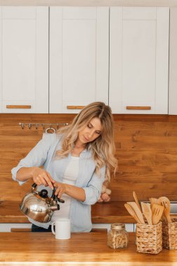 Genç ve mutlu bir kadın sabahları mutfakta kahve içiyor.