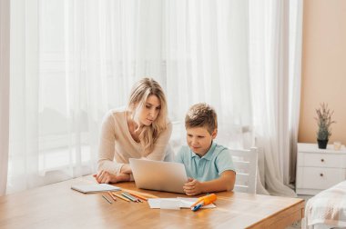 Annem küçük çocuğun ödevlerine yardım ediyor. Anne ve oğul birlikte çiziyor, anne ödevlerine yardım ediyor. Sevimli çocuk annesiyle birlikte okul ödevini yapıyor, evde, bir kitap yazıyor.