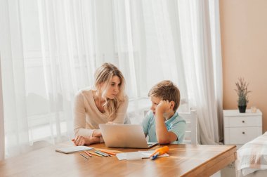 Annem küçük çocuğun ödevlerine yardım ediyor. Anne ve oğul birlikte çiziyor, anne ödevlerine yardım ediyor. Sevimli çocuk annesiyle birlikte okul ödevini yapıyor, evde, bir kitap yazıyor.