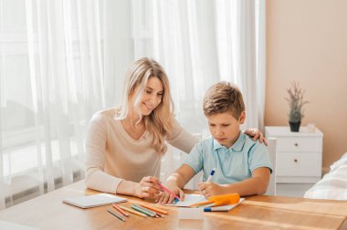 Gülümseyen anne, sevimli oğluna evde ödevlerini yapmasına yardım ediyor.