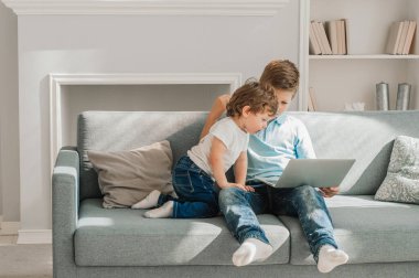 Oturma odasındaki kanepede oturan iki küçük kardeş kucağında dizüstü bilgisayarlarıyla online oyun oynuyorlar. Haftasonunu elektronik cihaz, kötü alışkanlık ve alet bağımlısı bir nesil kullanarak geçiren çizgi filmleri izliyorlar.