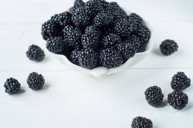 Taze böğürtlen, böğürtlen, nane yaprağı, beyaz kâse ve ahşap arka planda mavi kupa. Üst Manzara. Boşluğu kopyala