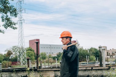 Panoya yazı yazan inşaat işçisi. Tulum ve turuncu kasklı inşaat metal bobini mağazasının yanında genç inşaat işçisi.