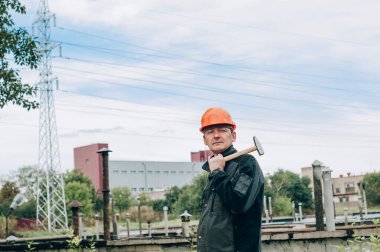 Panoya yazı yazan inşaat işçisi. Tulum ve turuncu kasklı inşaat metal bobini mağazasının yanında genç inşaat işçisi.