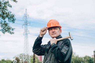 Panoya yazı yazan inşaat işçisi. Tulum ve turuncu kasklı inşaat metal bobini mağazasının yanında genç inşaat işçisi.