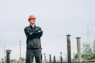 Tulum ve turuncu kasklı inşaat metal bobini mağazasının yanında genç inşaat işçisi.