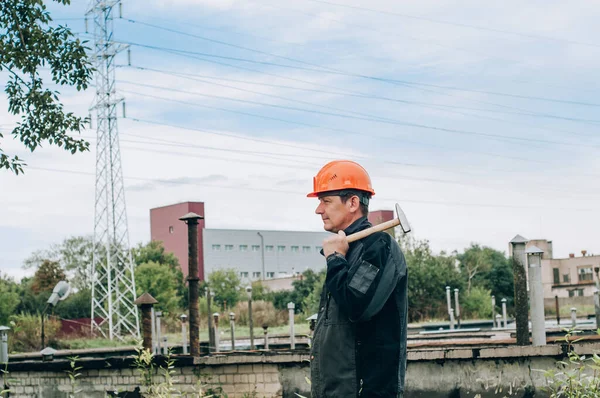 Panoya yazı yazan inşaat işçisi. Tulum ve turuncu kasklı inşaat metal bobini mağazasının yanında genç inşaat işçisi.