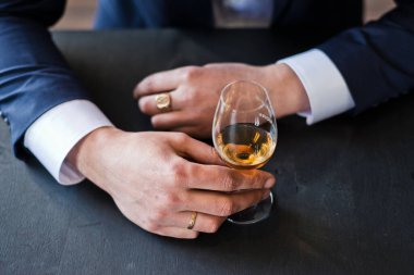 Damat bardağı viskiyle, eli bardakla yakın tutar.