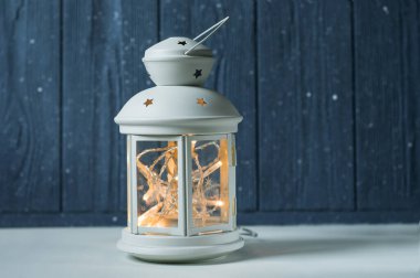 Beyaz, yanan mumları, ahşap masasında çam kozalakları ve arka planda parıltılı ışıkları olan klasik bir Fener. Noel arkaplanı. Mutlu yıllar. Seçici odak bütünlüğü.